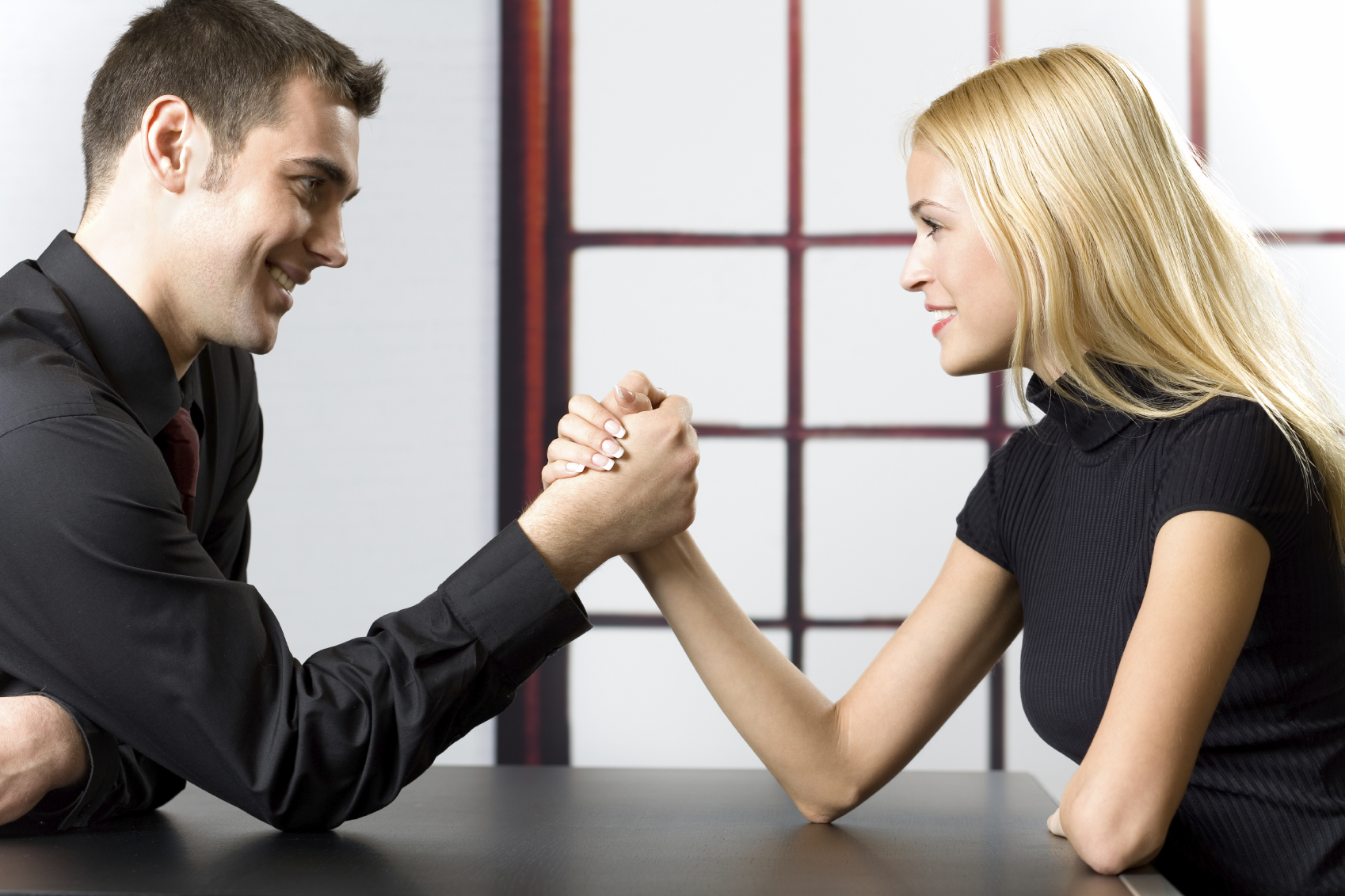 Young happy couple or business people fighting in arm-wrestling